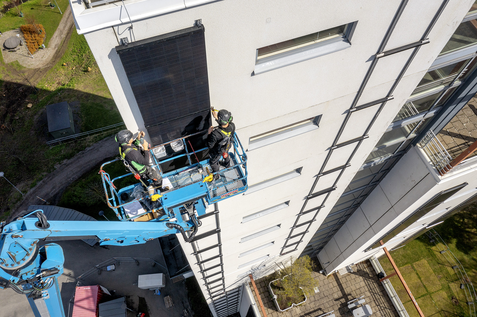 Två personer monterar solcellspaneler med skylift