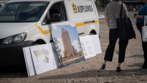 Tryckta bilder på hus och planlösningar står lutade mot en bil.